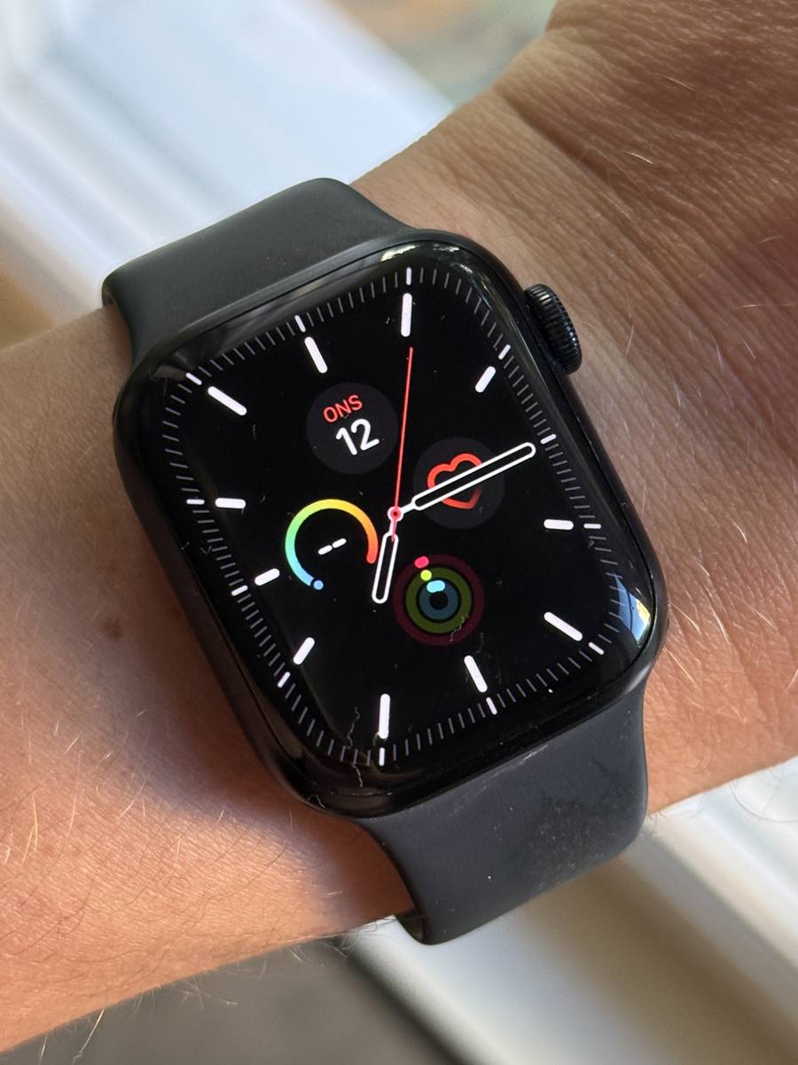 apple watch med svart sportband på en handled, urtavlan uppåt i dagsljus vid ett fönster