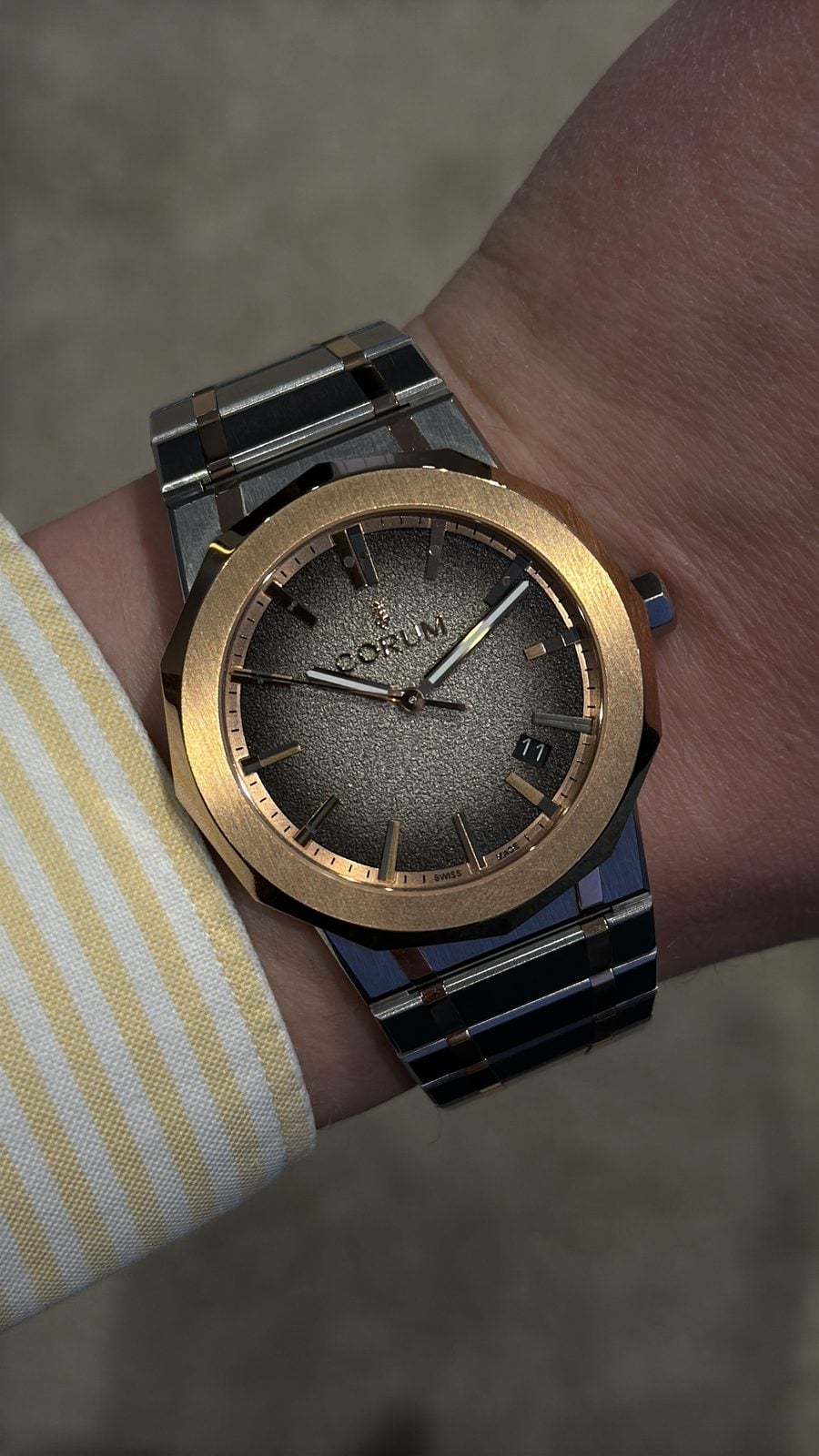 Corum admiral med lünett i roséguld och strukturerad grå urtavla på tvåfärgat armband på handleden corum admiral med lünett i roséguld och strukturerad grå urtavla på tvåfärgat armband på handleden