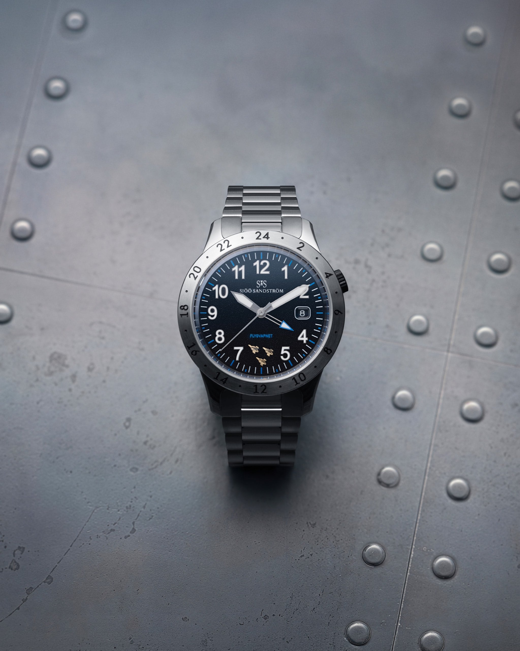sjöö sandström annual edition 2026 royal steel worldtimer mot en nitad flygplansplåt