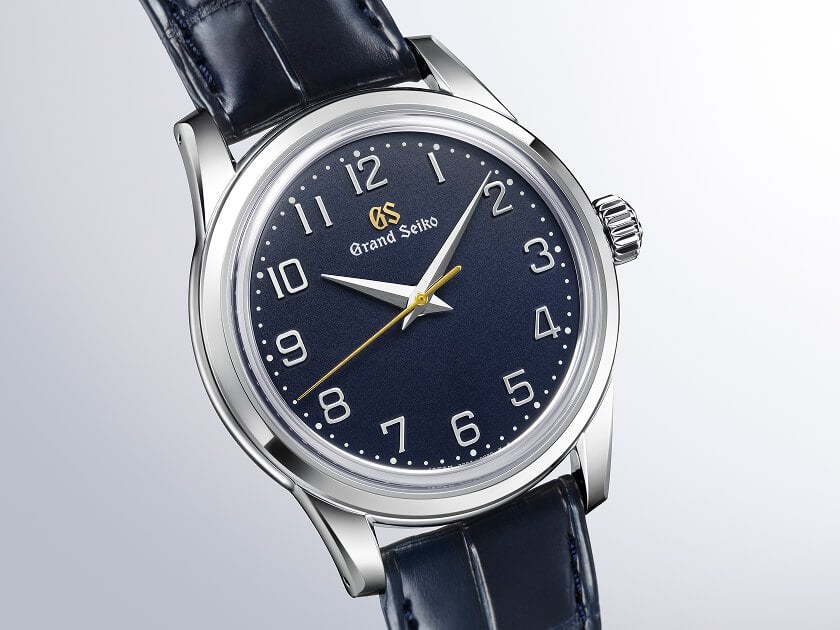 närbild på grand seiko classic blue arabic med arabiska siffror och marinblå urtavla på blått krokodilarmband